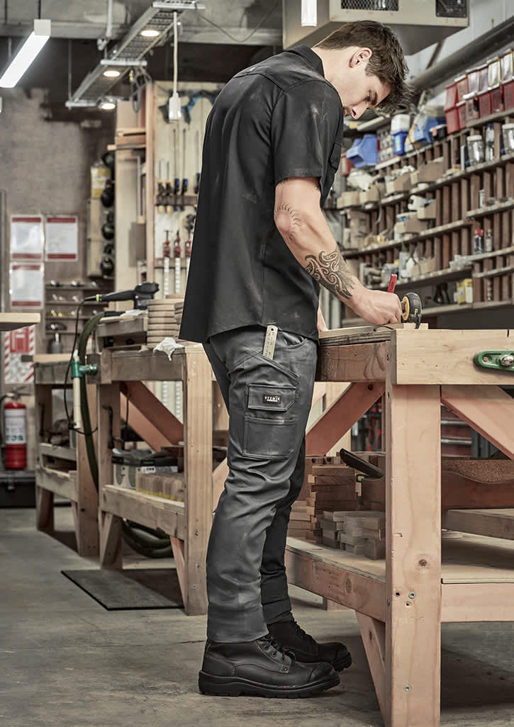 A man in black cargo pants and a black shirt standing at a workbench in a workshop, focused on a task. Mens Essential Basic Stretch Cargo Pant - Image 1