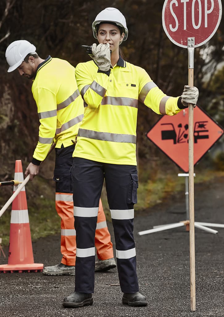 Two individuals in high-visibility workwear, one holding a stop sign. The clothing is bright yellow with reflective stripes. Womens Bio Motion Taped Pant - Image 1