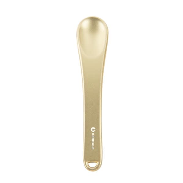A gold metal cosmetic spatula with a smooth, rounded end and a branding logo on the handle. Metal Cosmetic Spatula - Image 1