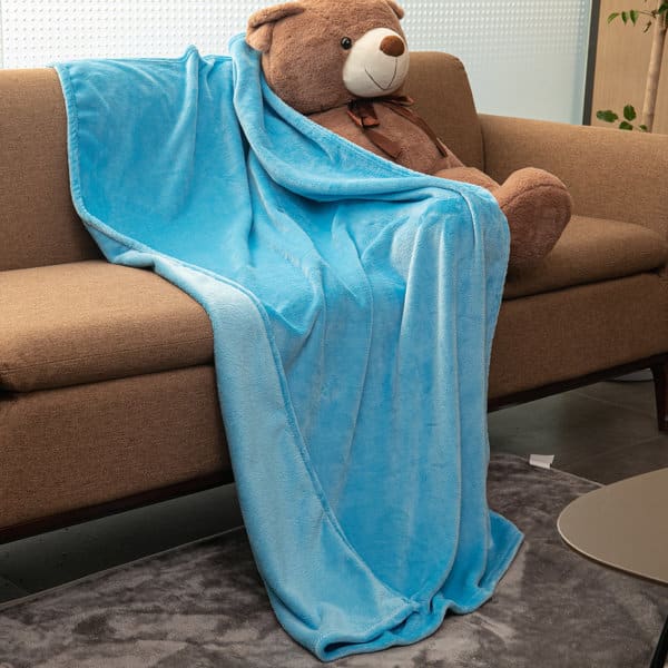 A blue flannel fleece throw blanket draped over a couch, partially covering a large teddy bear. Flannel Fleece Throw Blanket - Image 1