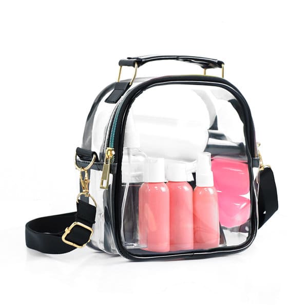 A clear crossbody purse with black and white accents, featuring several pink and white containers inside. TPU Clear Crossbody Purse For Womon - Image 1