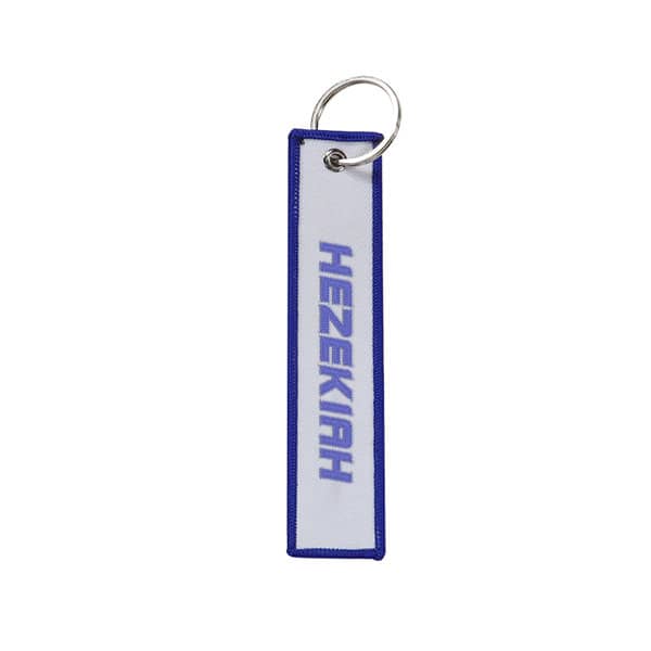 A custom woven label keychain featuring a blue and white design with a circular keyring. It has a logo. Custom Woven Label Keychain - Image 1