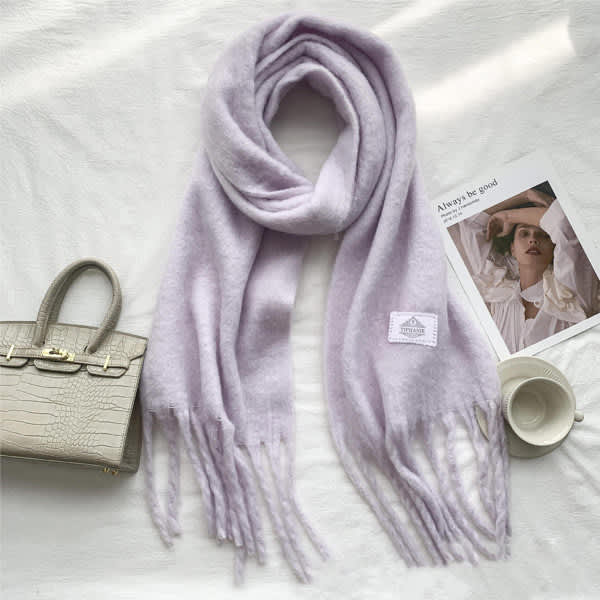 A lilac wool scarf with tassels, featuring a small logo, laid out beside a handbag and a magazine. Tassel Wool Scarf - Image 1