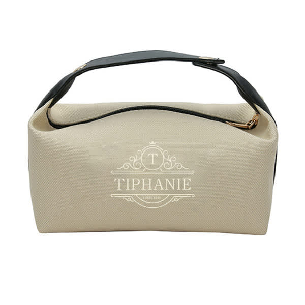 A portable toiletry storage bag in cream and black, featuring a top handle and a logo. Portable Toiletry Storage Bag - Image 1