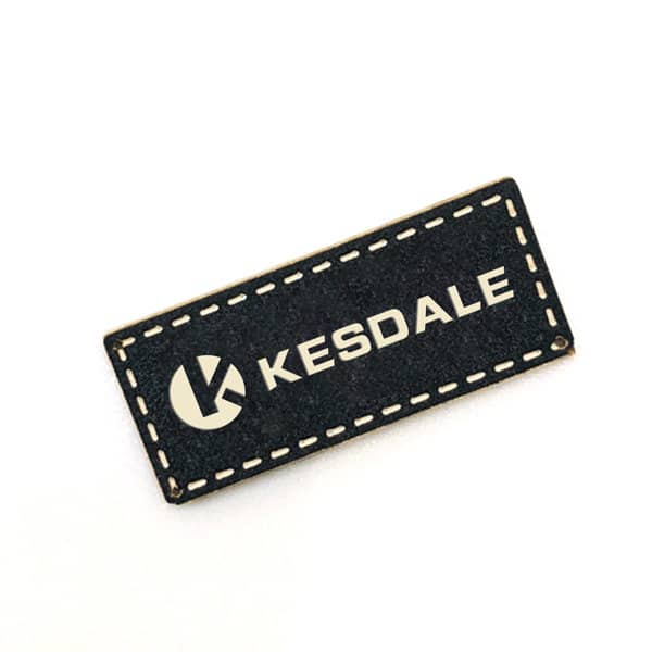 A black custom PU leather label with a stitched border and a logo. It features the text "KESDALE" in white. Custom PU Leather Label - Image 1