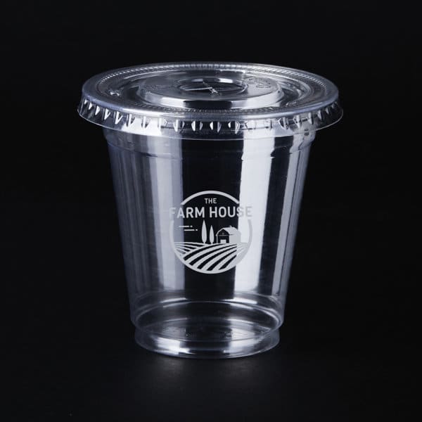 A clear 9 oz. PET cup with a lid, featuring a logo, set against a black background. 9 oz. Clear PET Cup With Lid - Image 1