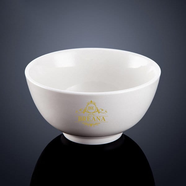 A white melamine salad bowl with a rounded shape and a gold logo at the base, set against a dark background. 5 Inch Melamine Salad Bowl - Image 1