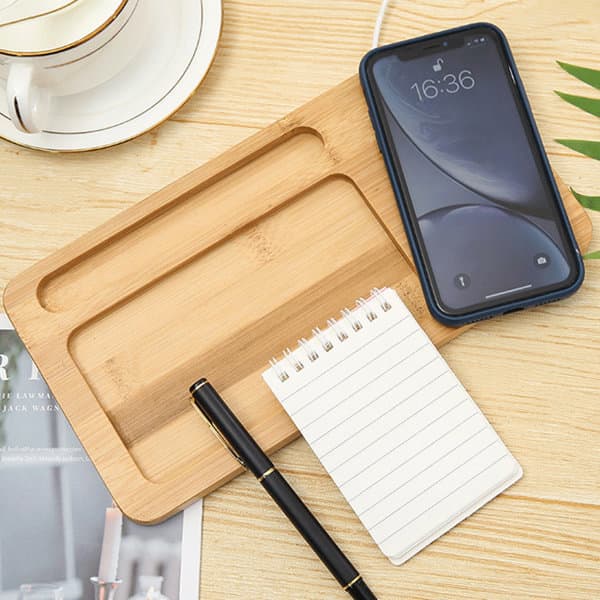 A bamboo desktop organiser featuring a phone slot, a notepad, and a pen, set on a wooden surface with a cup in the background. Bamboo Desktop Organizer Wireless Charging Pad - Image 1
