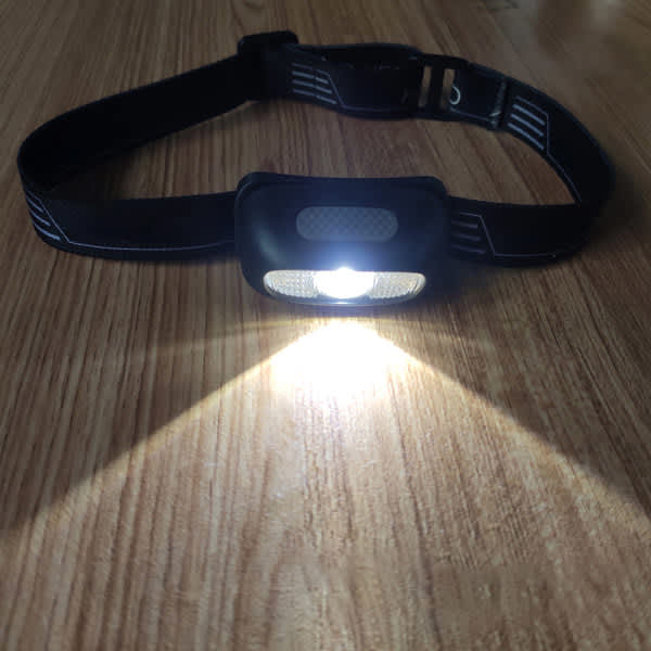 A black LED rechargeable headlamp with a bright light beam, featuring an adjustable head strap. LED Rechargeable Headlamp - Image 1