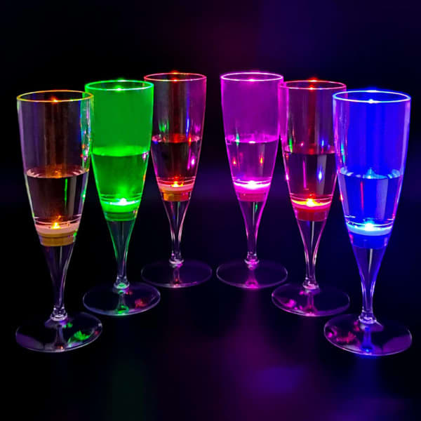A set of seven LED light up champagne glasses in vibrant green, pink, and blue, glowing against a dark background. LED Light Up Champagne Glasses - Image 1