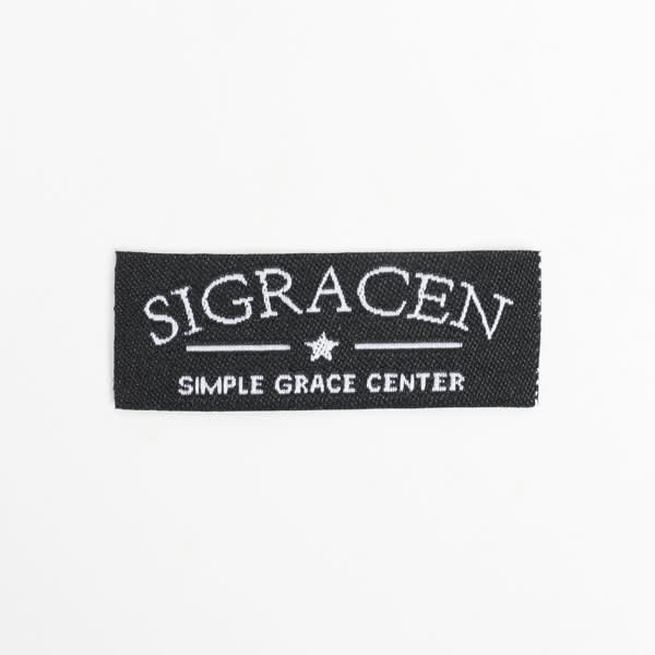A black woven sewing label featuring white embroidered text and a star design. Personalized Woven Sewing Label - Image 1