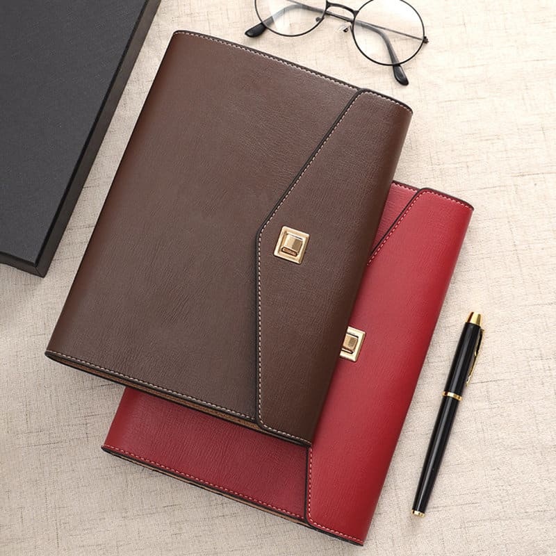 A brown and red PU leather trifold envelope padfolio, featuring a sleek design and a logo. A pen and glasses are nearby. PU Leather Trifold Envelope Padfolio - Image 1
