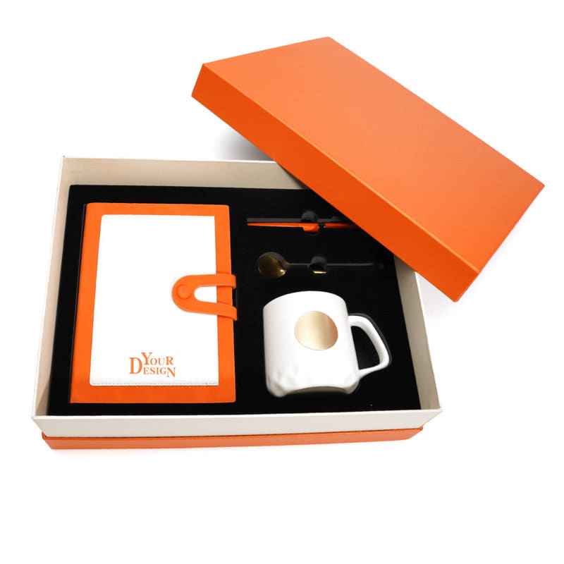 A notebook with an orange cover, a ceramic cup with a gold spot, a pen, and a spoon in an orange box. Notebook Set With Ceramic Cup - Image 1