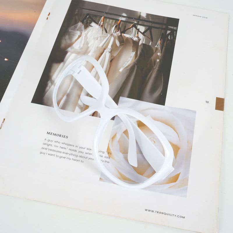 An oversized vintage eyeglasses frame in white, placed on a magazine featuring a soft floral image. Oversized Vintage Eyeglasses Frame - Image 1